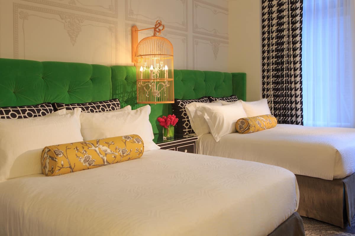 Two beds with green headboards, white bedding, and a decorative birdcage light fixture.