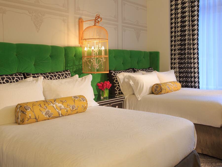 Two beds with green headboards, white bedding, and a decorative birdcage light fixture.