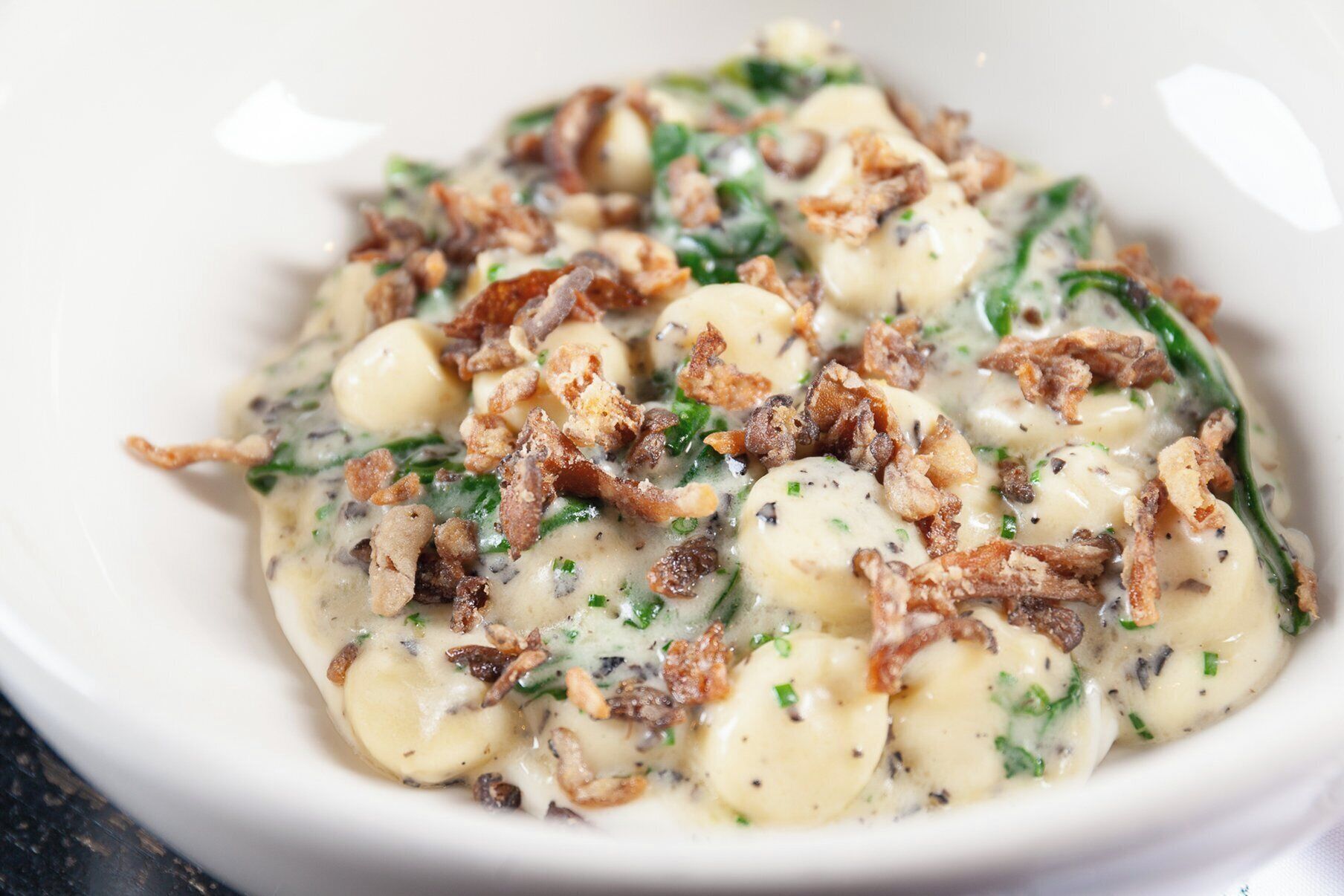 A bowl of creamy pasta with bacon bits and herbs.