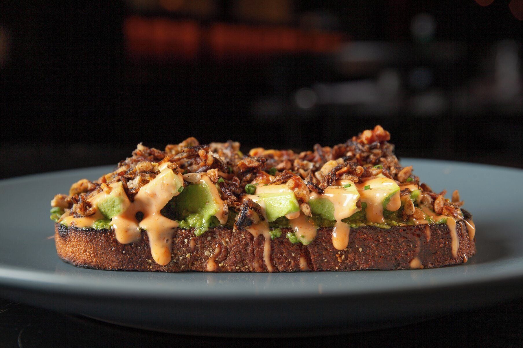 A plate with a food item topped with avocado, green vegetables, and a creamy sauce.