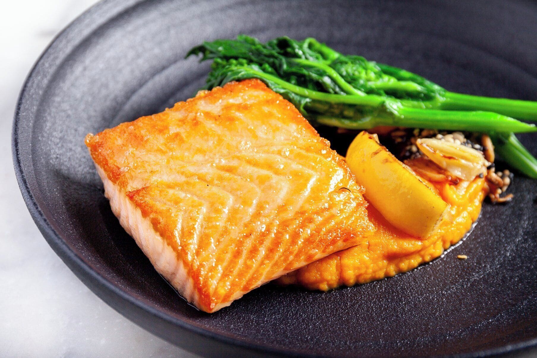 Um prato com salmão, uma fatia de limão e legumes verdes.