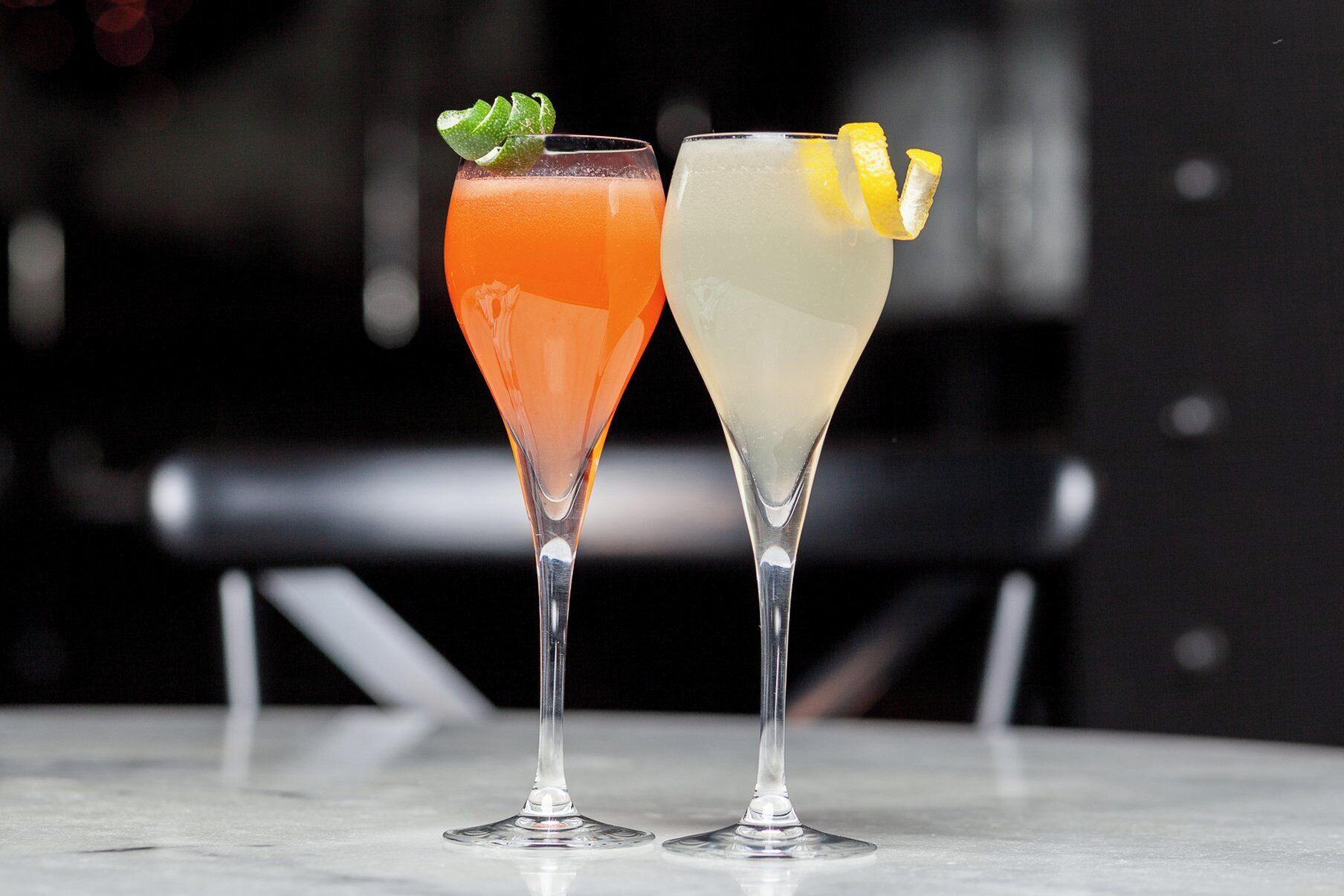 Two glasses of cocktails on a marble surface with a blurred background.