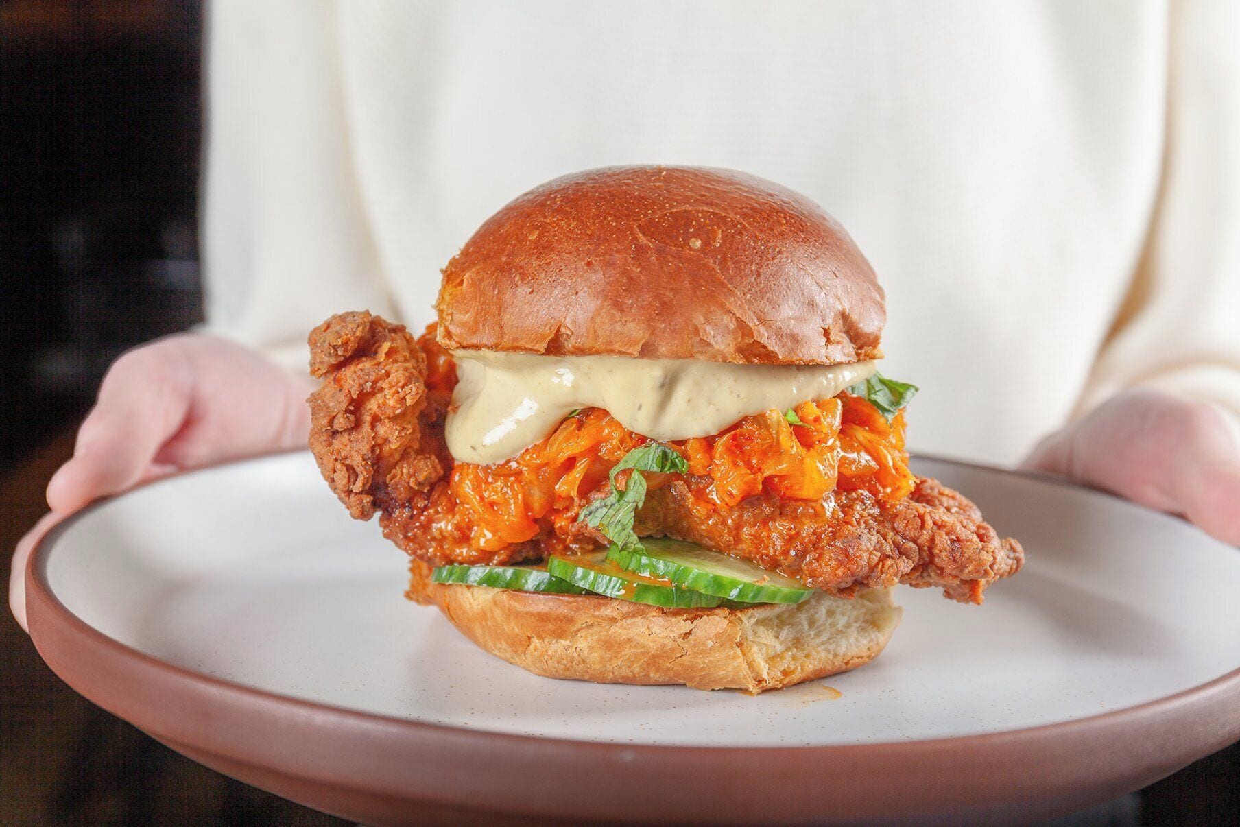 A sandwich with a bun, chicken, sauce, and greens on a plate.