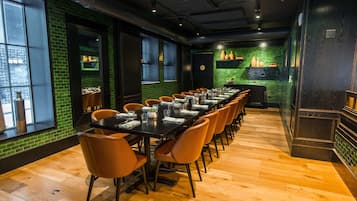Una larga mesa de comedor con sillas, un muro de ladrillo y una zona de cocina con estanterías.