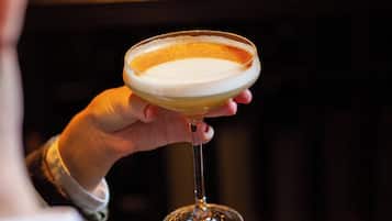 A hand holding a cocktail glass with a creamy top layer, likely a frothy drink.