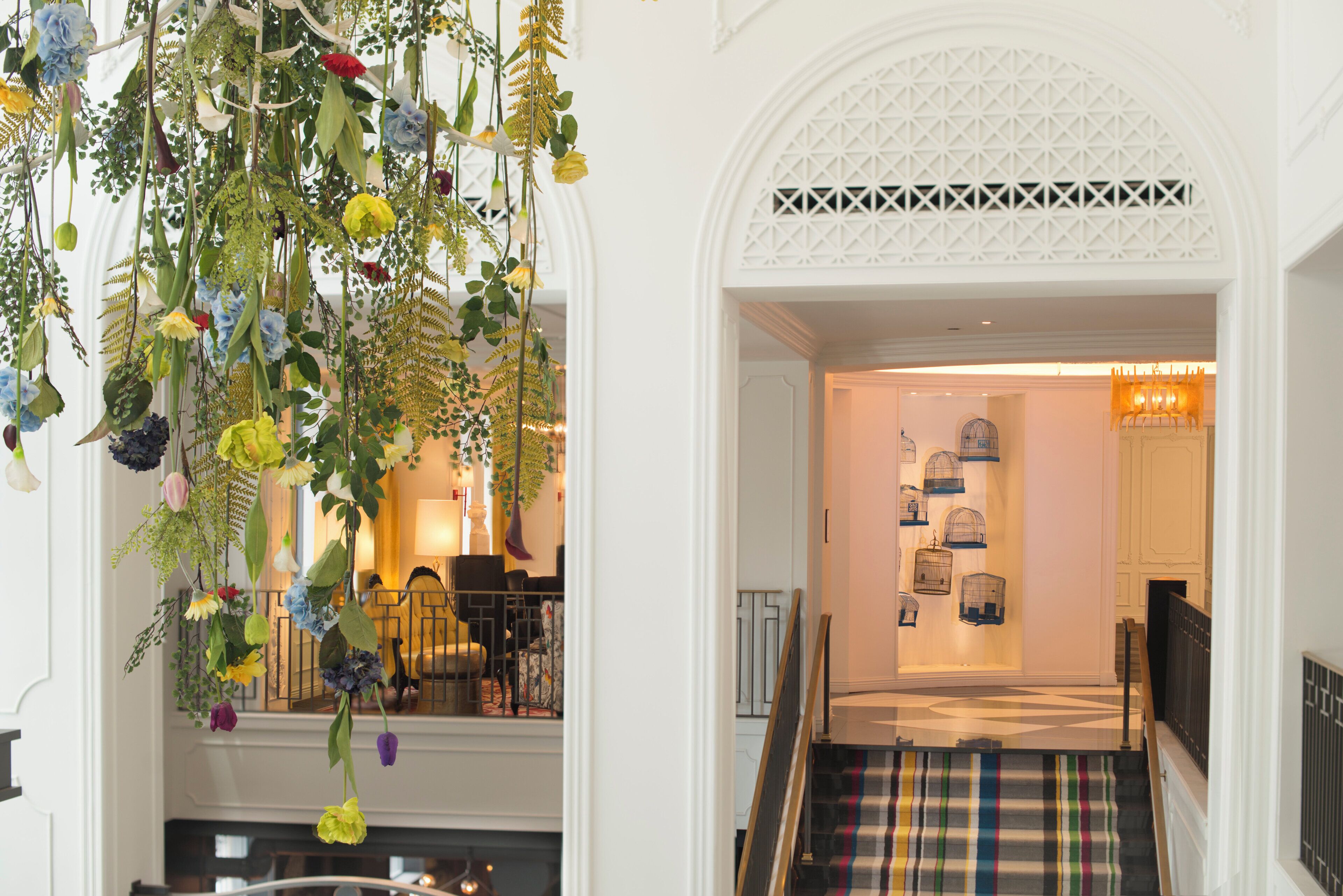 A hotel lobby with a staircase, a hanging floral arrangement, and a display of birdcages.