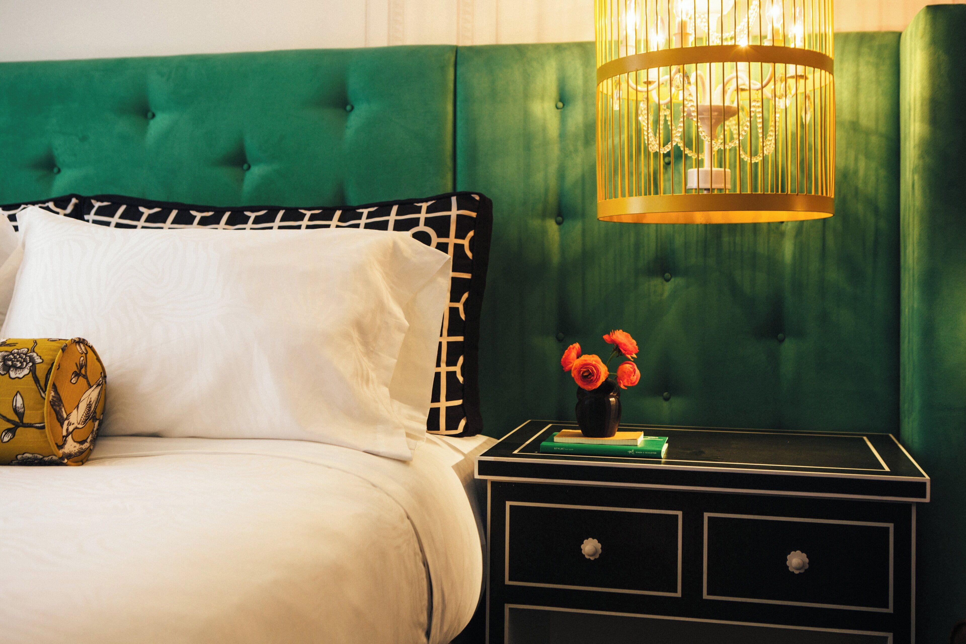 A bed with a white pillow and a decorative pillow, a nightstand with a vase of flowers, and a green upholstered headboard.