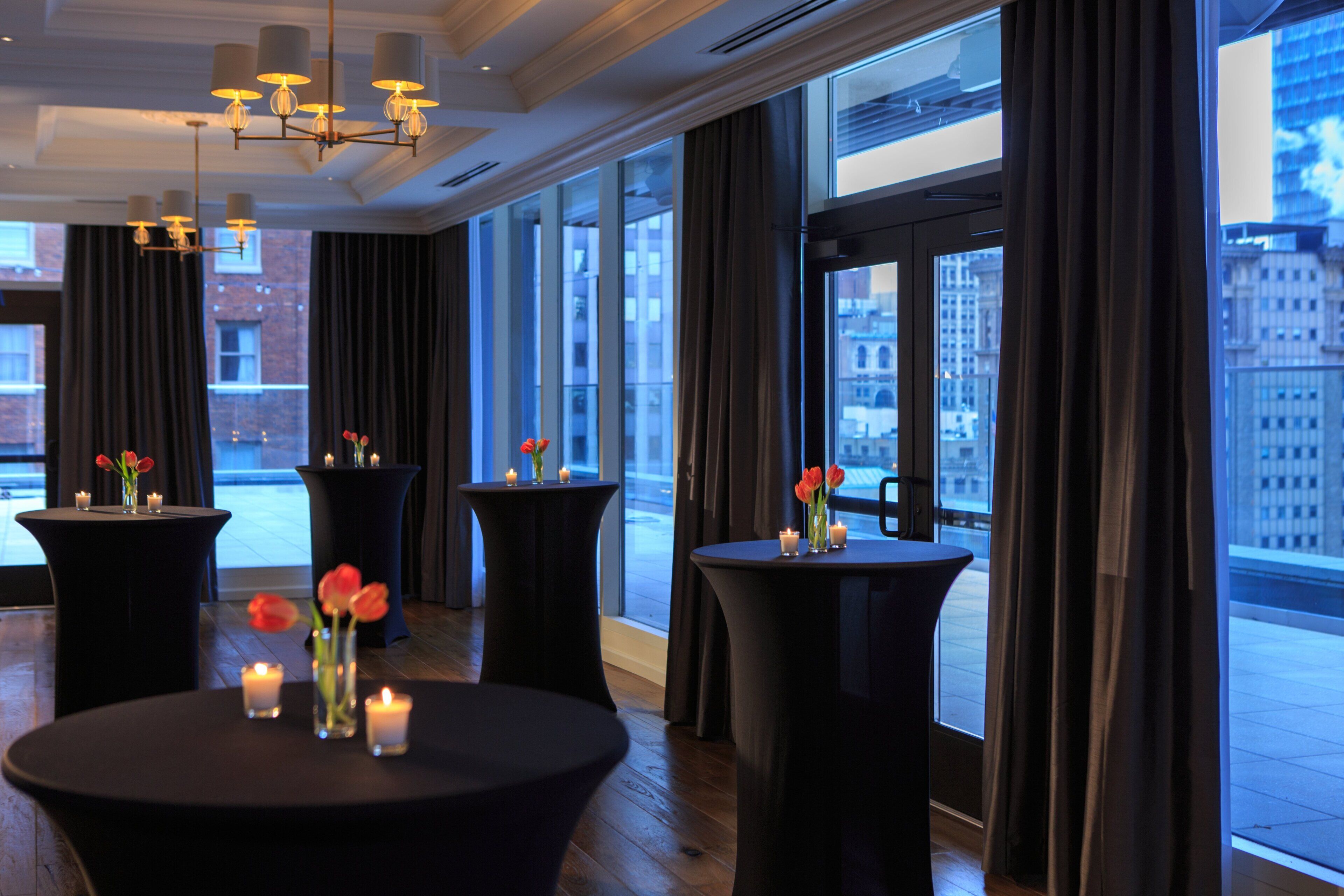 A modern hotel lobby with large windows, round tables with candles, and a city view.