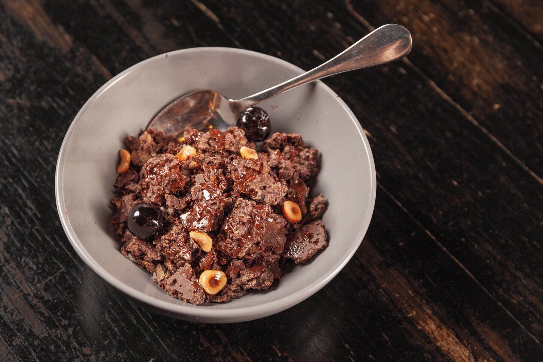 A bowl of food with a spoon on a dark wooden surface.