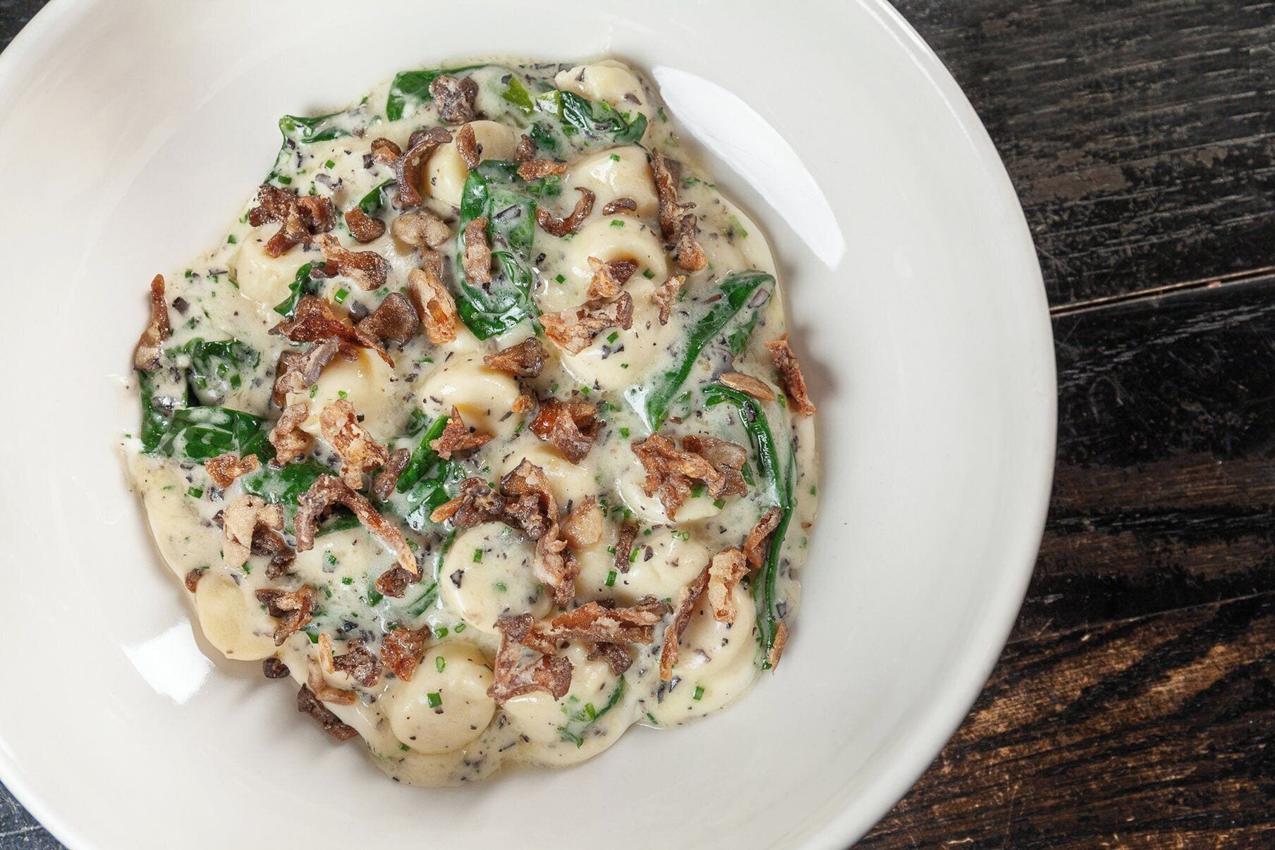 A white plate with a creamy dish containing green vegetables and crispy elements, on a dark wooden surface.