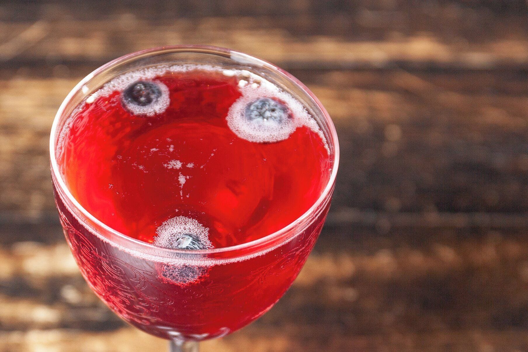 Un vaso con líquido rojo y burbujas, posiblemente un cóctel, sobre una superficie de madera.