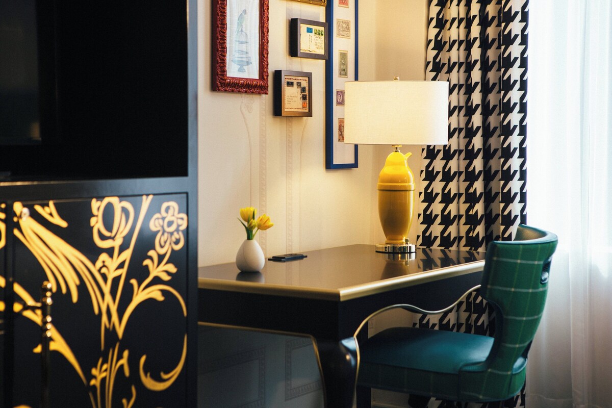 A hotel room with a desk, a lamp, a chair, and a decorative panel.