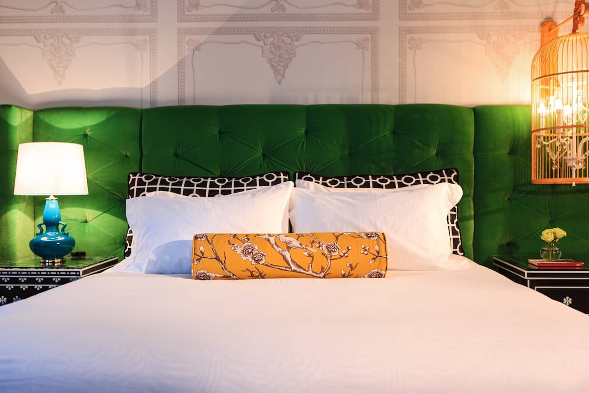 A bed with a green upholstered headboard, white bedding, and a decorative pillow.