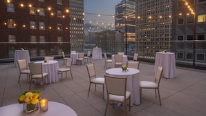 A rooftop terrace with round tables and chairs, string lights, and a city view. - Kimpton Hotel Monaco Pittsburgh by IHG (Pittsburgh)