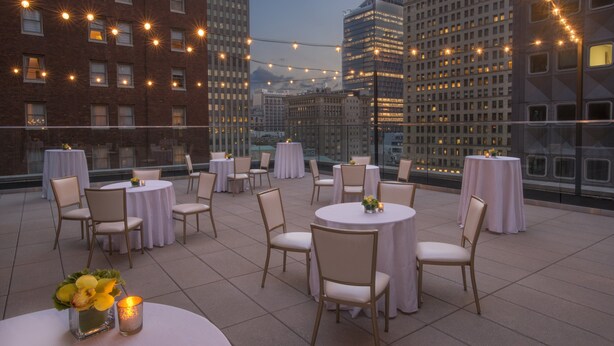 Una terrazza sul tetto con tavoli e sedie rotonde, luci decorative e vista sulla città.