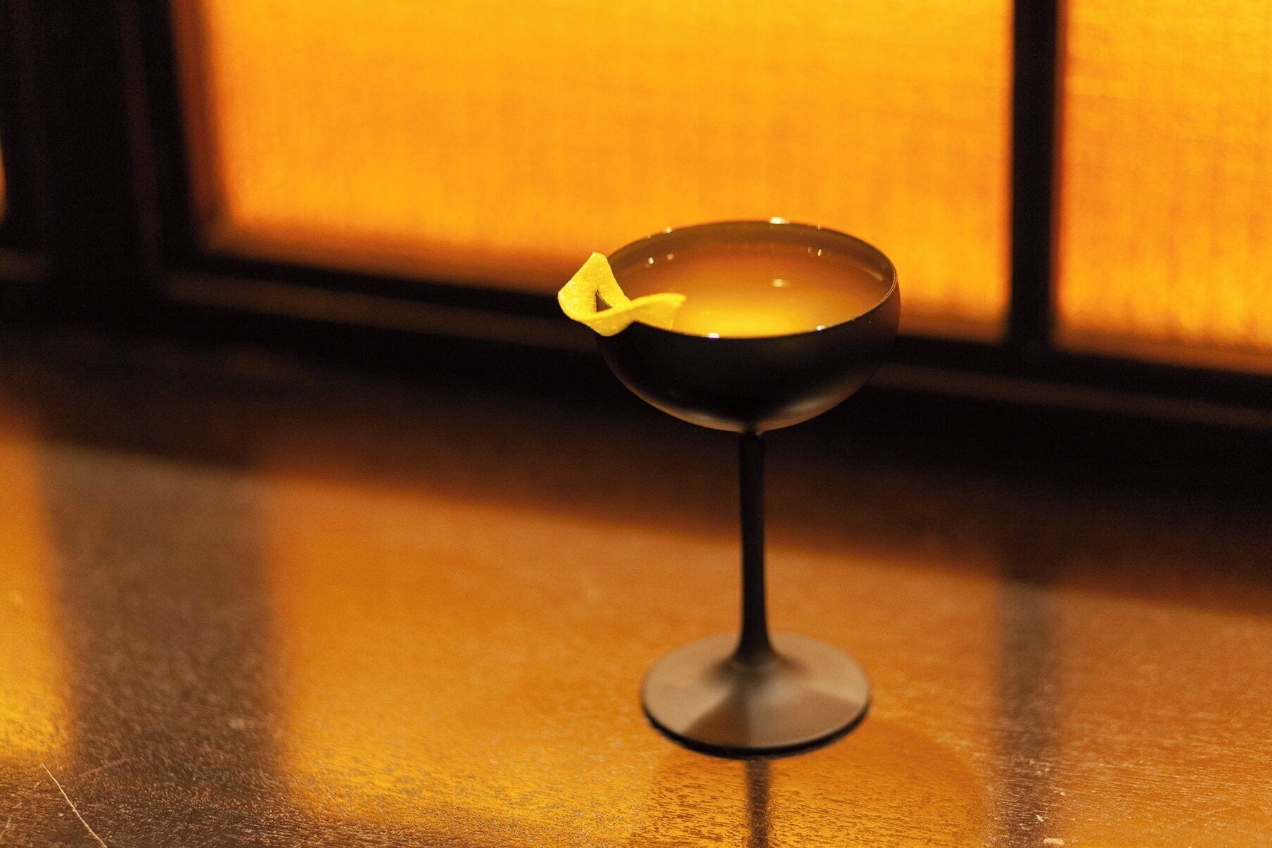 Et cocktailglas med et citronskive på en spejlende overflade.