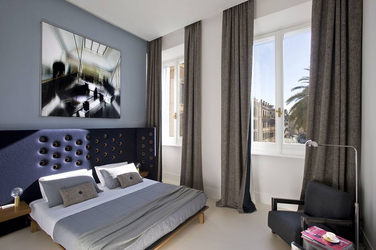 A modern bedroom with a bed, a chair, a large window, and a painting on the wall.