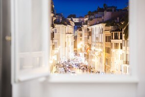 A view of a brightly lit street with historic buildings, a crowd of people, and cars.