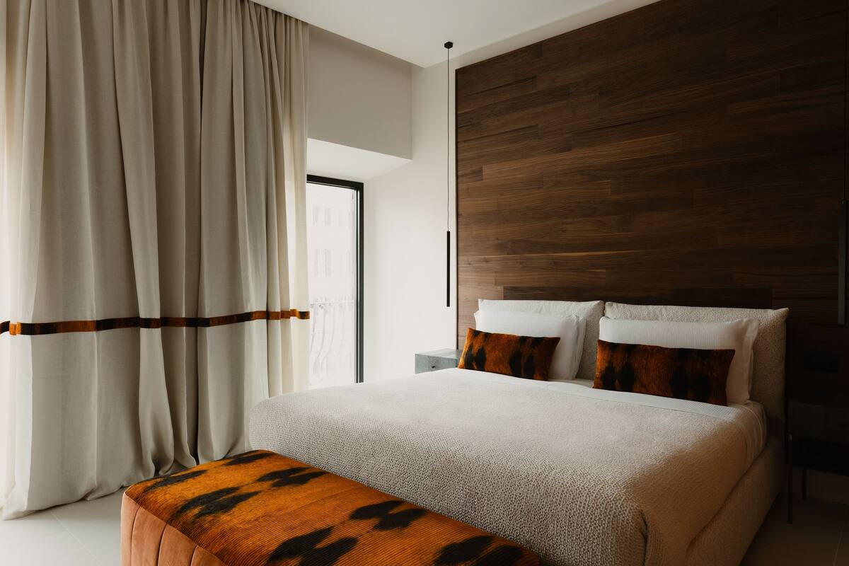 A modern bedroom with a large bed, wooden headboard, and a bench.