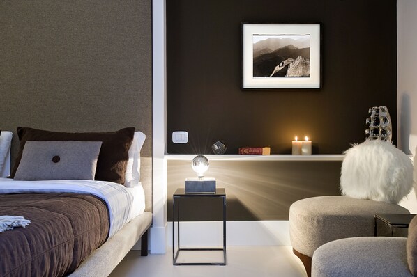A modern bedroom with a bed, bedside table, and a nightstand with a lamp.