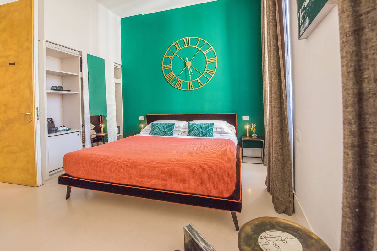 A bedroom with a large bed, a green wall clock, and a wardrobe.