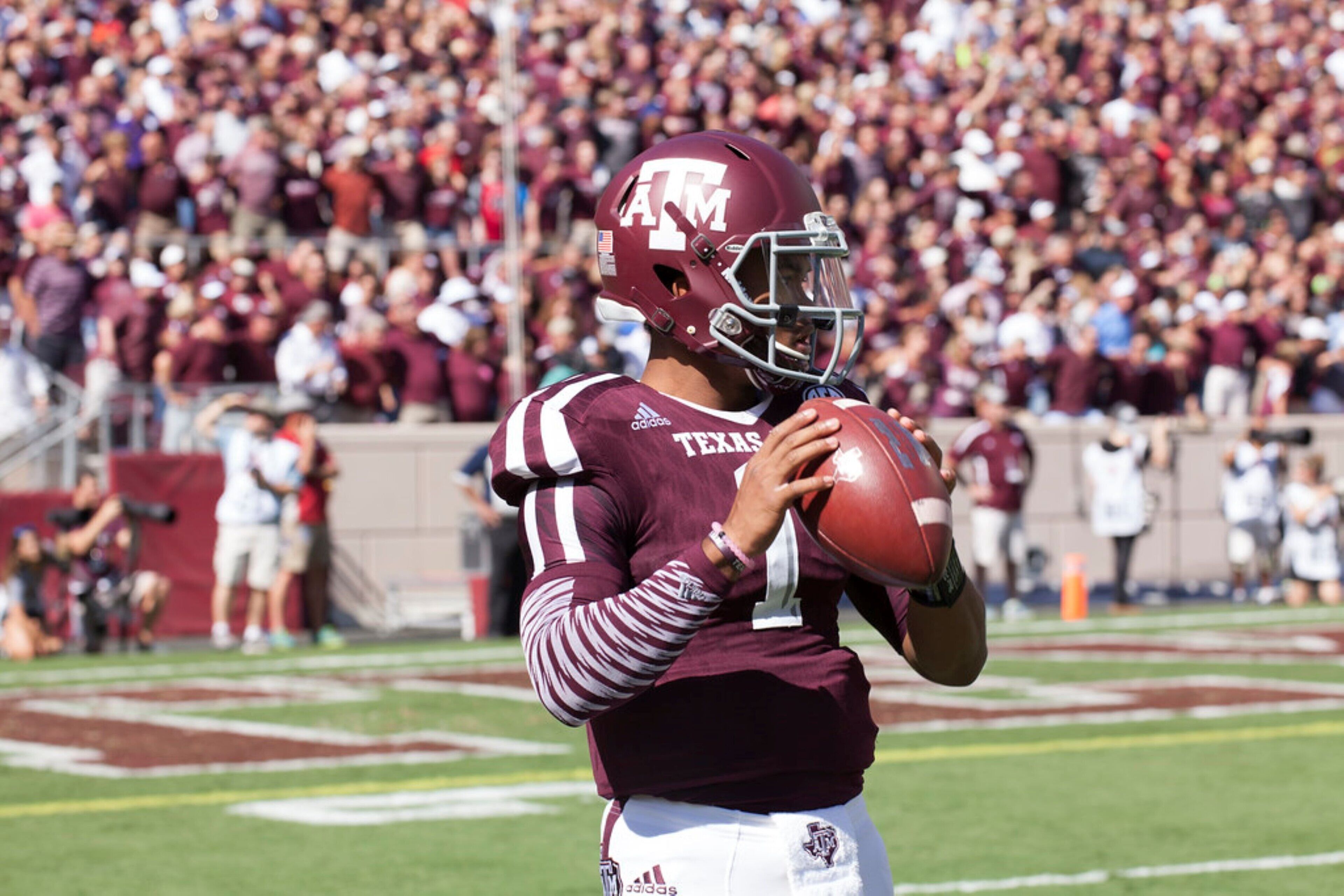 A football player in a maroon and white uniform holding a football on a field.