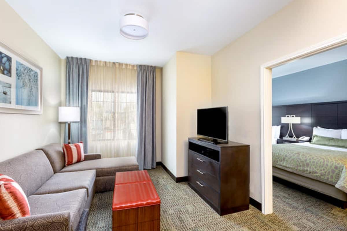 A hotel room with a sofa, a television on a cabinet, a bed with a headboard, and a window with curtains.