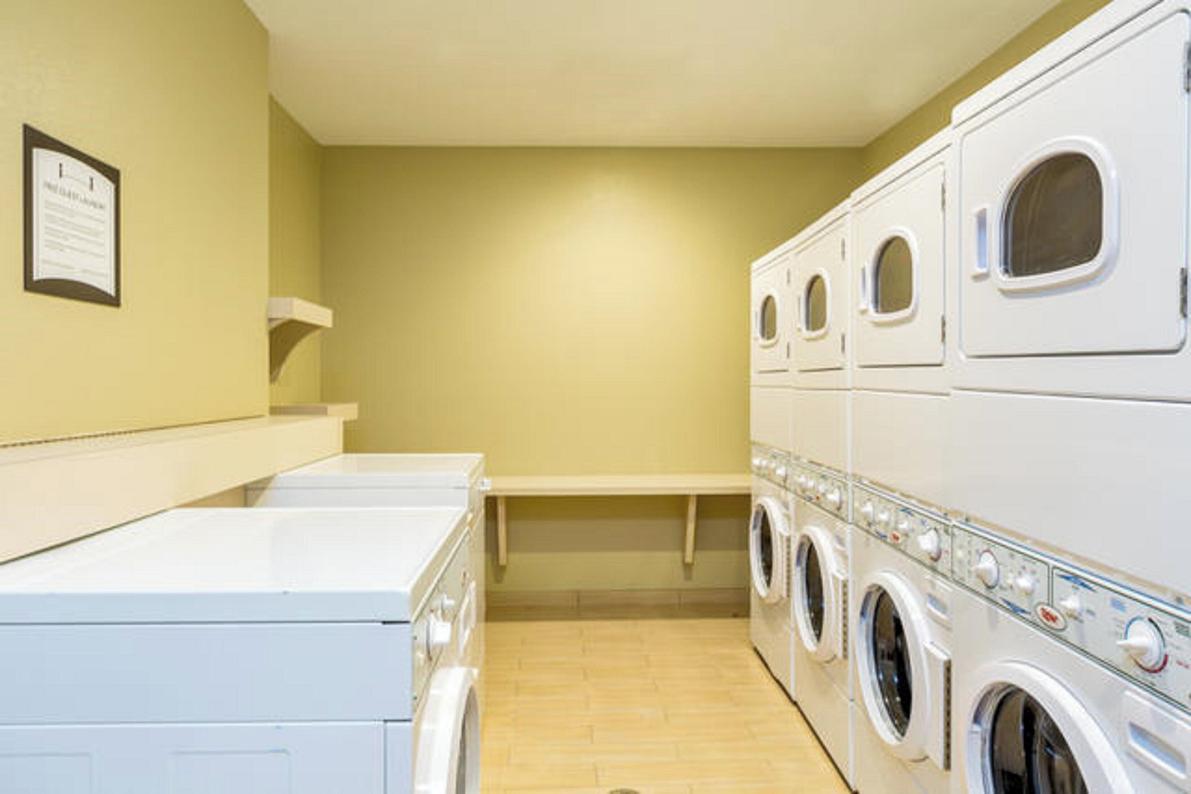 A laundry room with stacked washers and dryers, a bench, and a wall-mounted sign.
