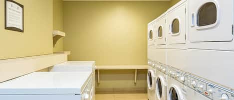 A laundry room with stacked washers and dryers, a bench, and a wall-mounted sign.