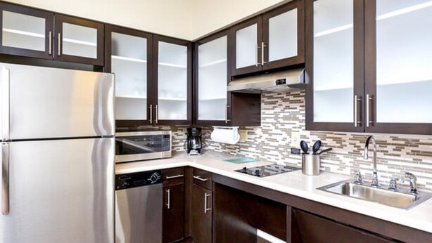 A modern kitchen with dark wooden cabinets, stainless steel appliances, and a tiled backsplash. - Staybridge Suites College Station by IHG (College Station)
