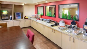Una cocina moderna con una mesa de madera, un muro decorado en rojo y varios electrodomésticos como una cafetera y un tostador.