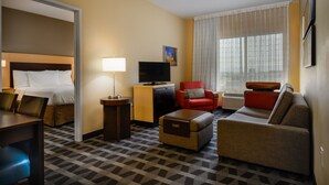 Una habitación de hotel con cama, televisión, un sillón rojo, sofá y alfombra estampada.