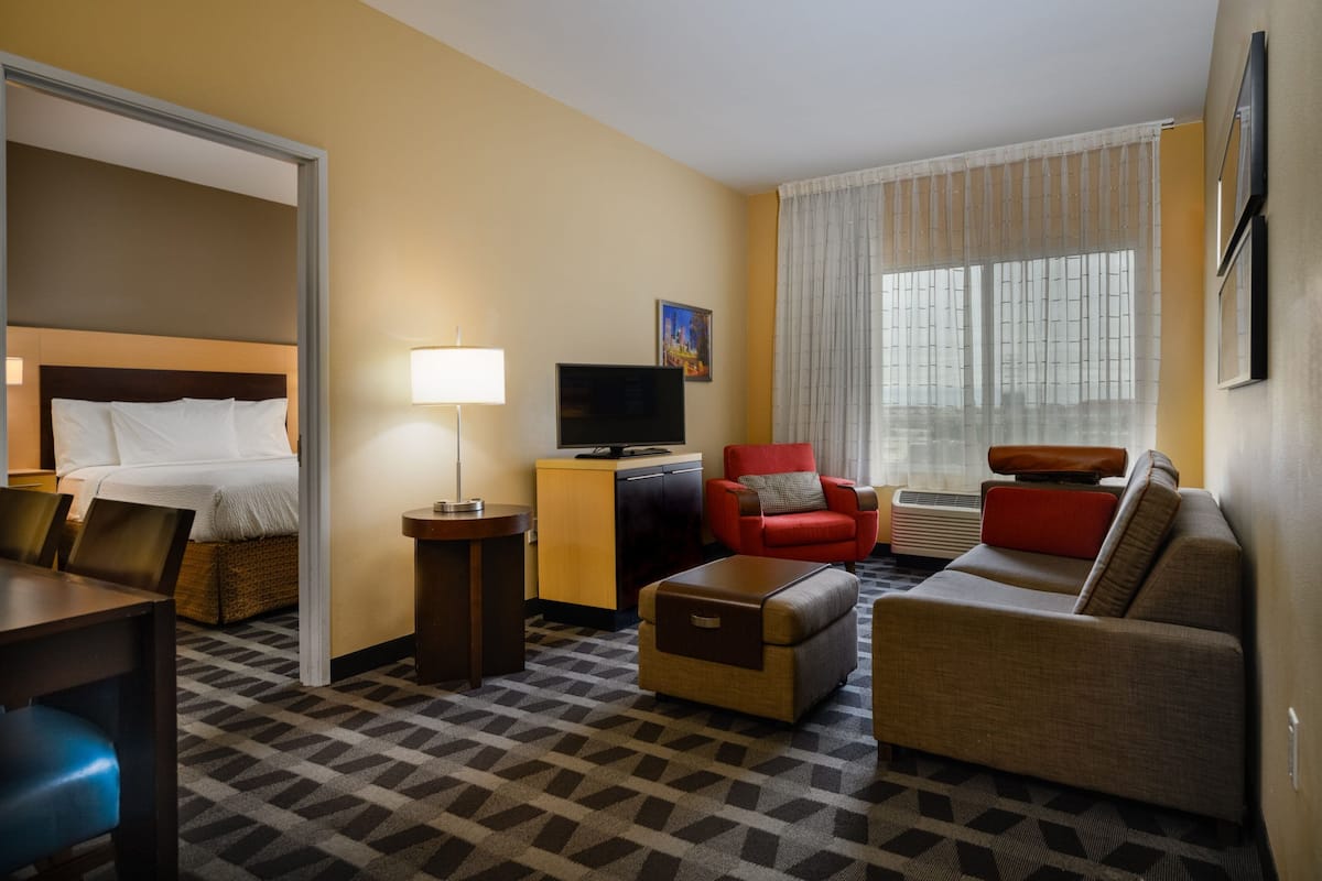 Ein Hotelzimmer mit einem Bett, einem Fernseher, einem roten Sessel, einer Couch und einem gemusterten Teppich.