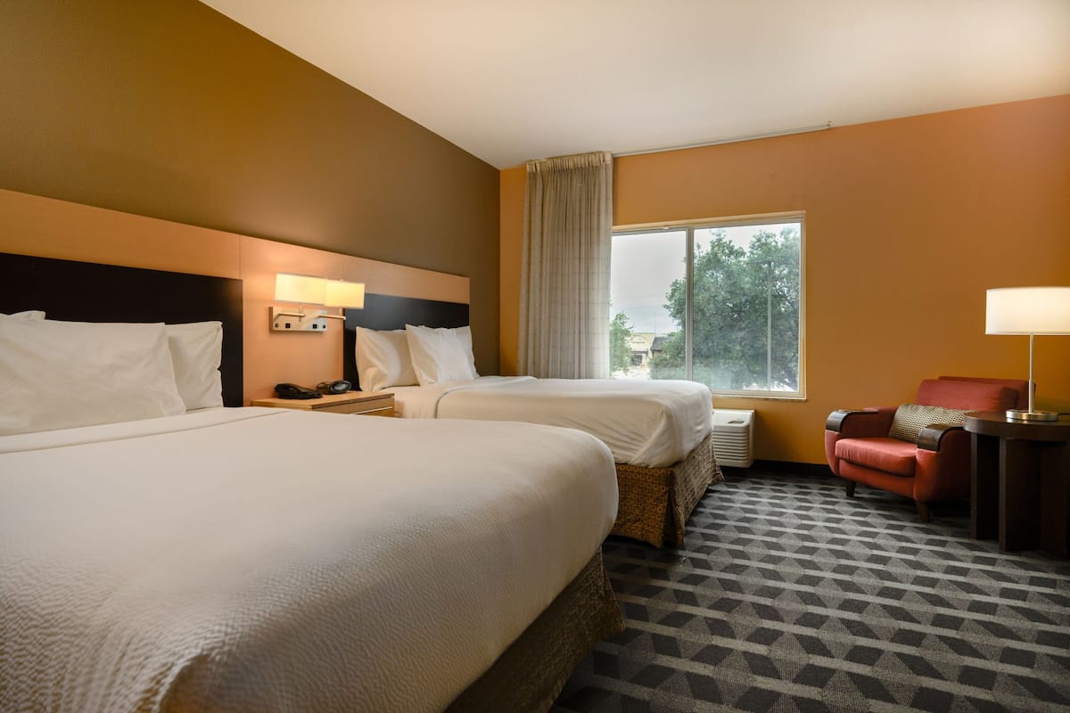 Ein Hotelzimmer mit zwei Betten, einem kleinen Sofa, einem Schreibtisch und einem Fenster mit Blick auf Bäume.