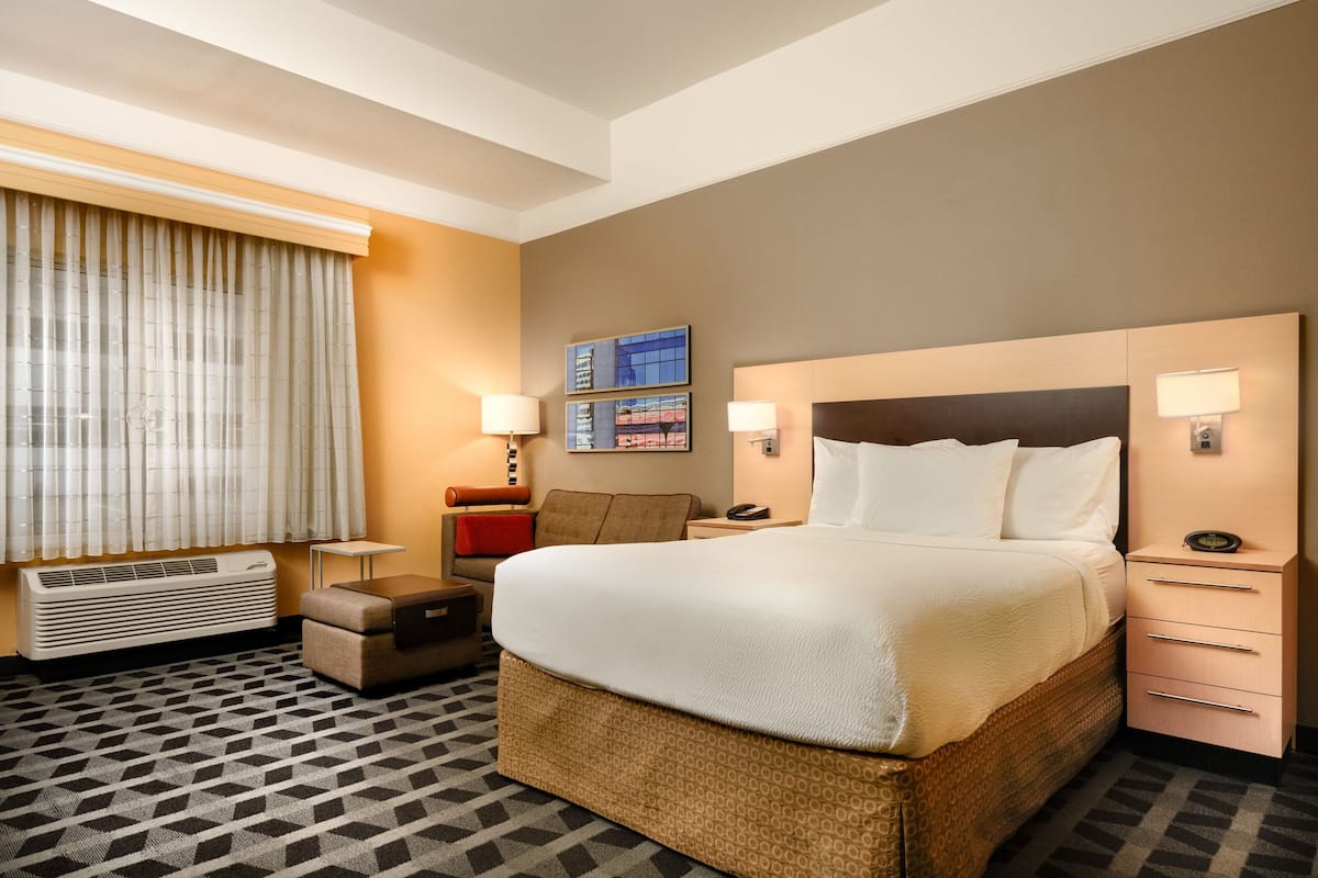 Ein Hotelzimmer mit einem großen Bett, Nachttischlampen, einem kleinen Tisch, einem Stuhl und einem Fenster mit Vorhängen.