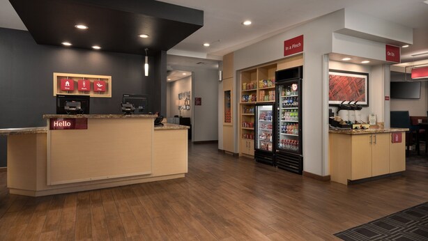 Zona de recepción de un hotel con mostrador de recepción, un refrigerador lleno de bebidas y una máquina de café.