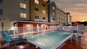Un hotel con piscina, sillones de descanso y una zona cubierta con sombrillas.