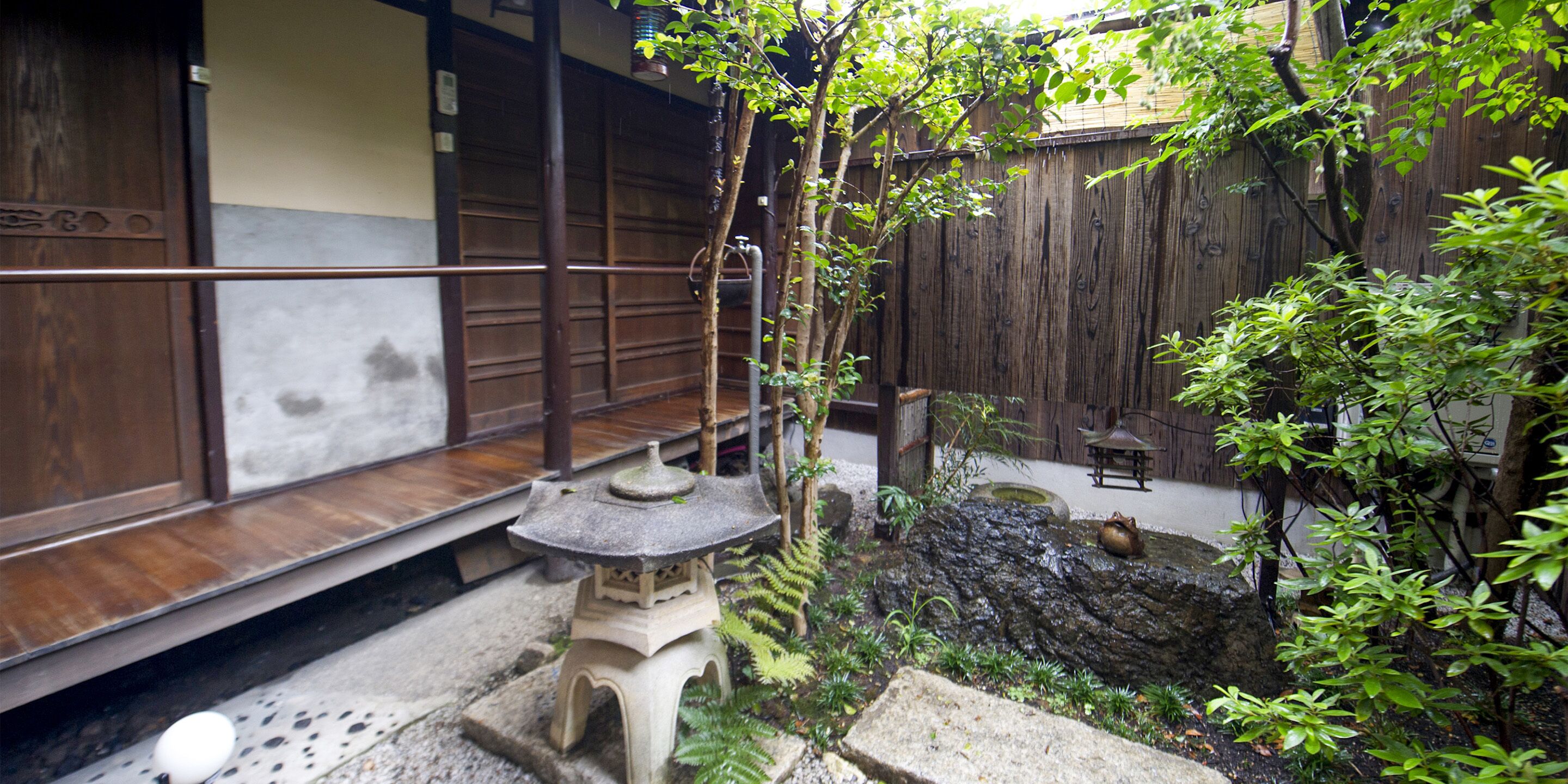Een traditionele Japanse tuin met een stenen lantaarn, een klein vijvertje en een houten omheining.