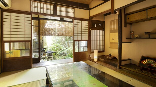 Una habitación japonesa tradicional con suelo de tatami, puertas correderas y vistas a un jardín.
