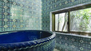 Un baño con una bañera azul grande, azulejos estampados y una ventana con vistas a la vegetación.