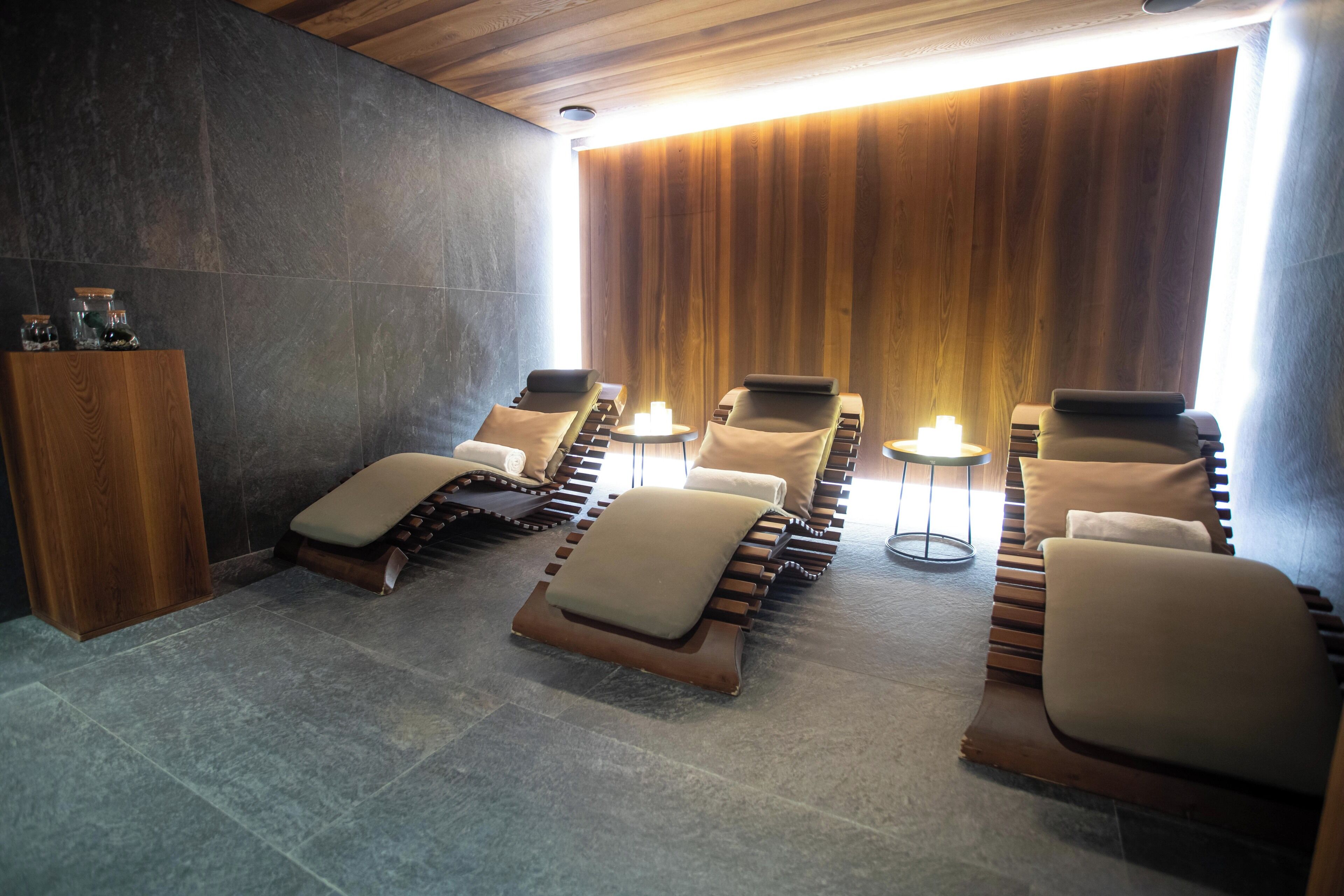 A spa room with massage chairs, a wooden cabinet, and a stone wall.