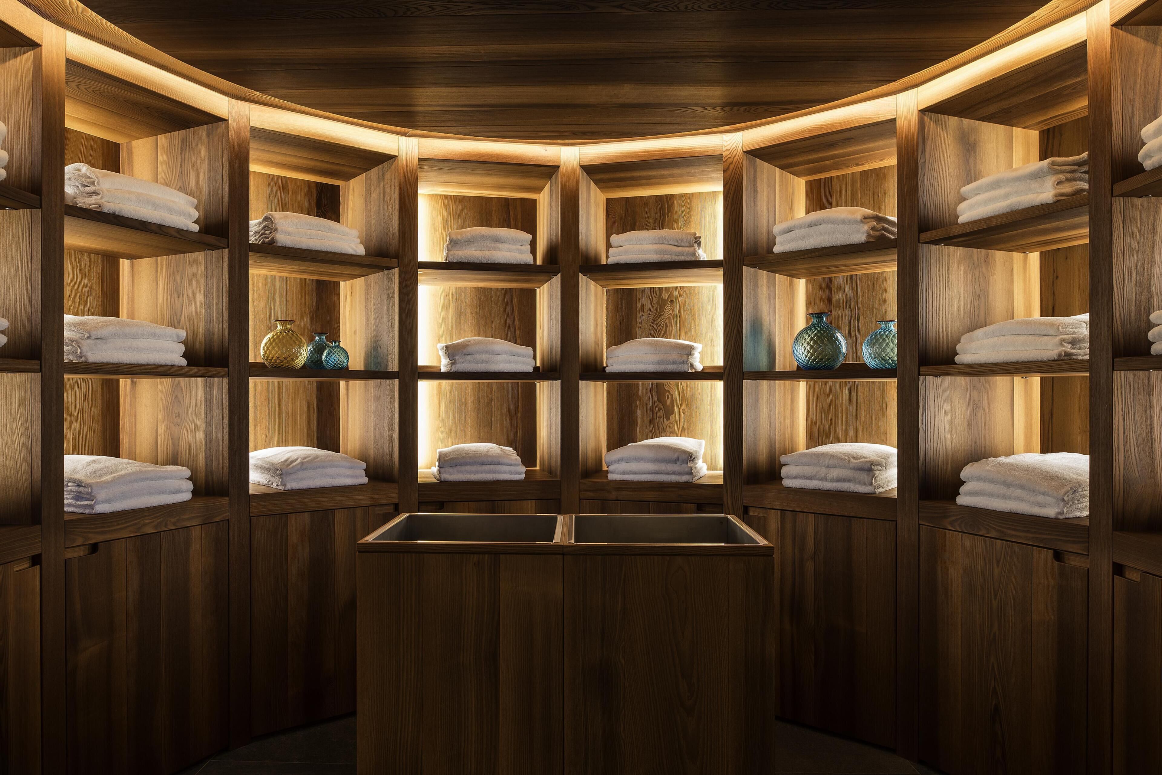 A wooden interior with shelves holding towels and decorative vases.
