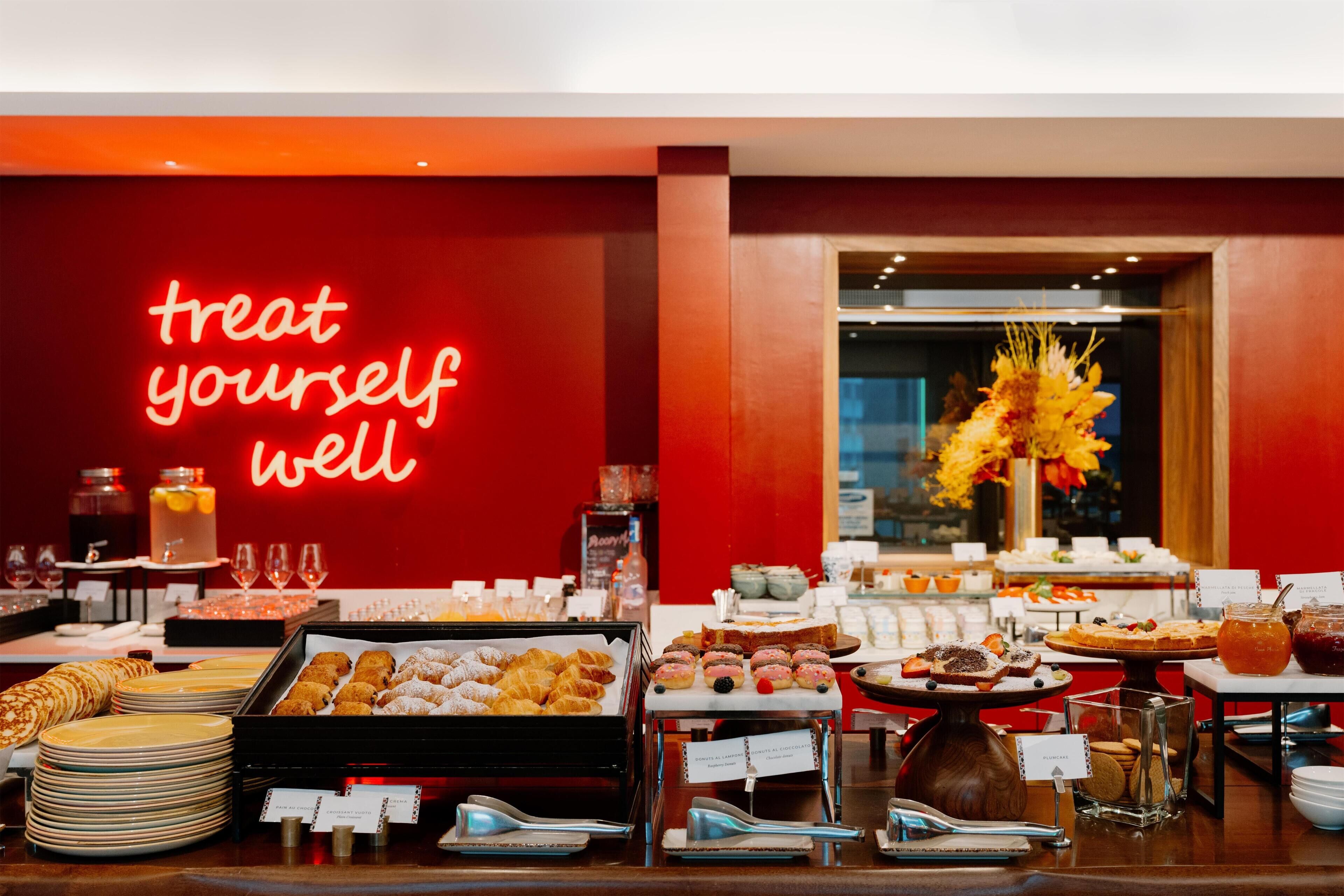 A buffet with various food items and a neon sign that reads 'treat yourself well'.