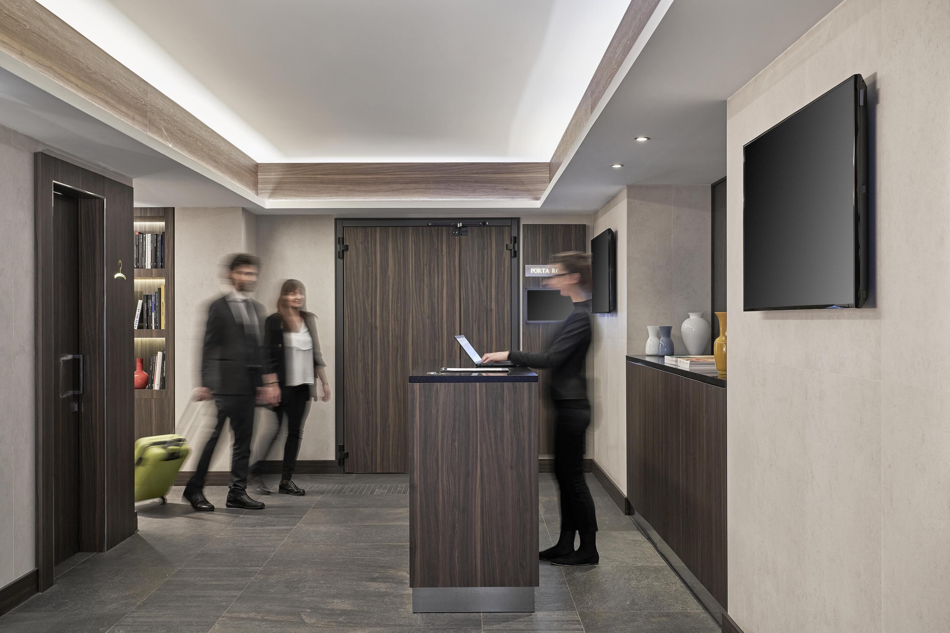 A modern lobby with a reception desk, a flat-screen TV, and a bookshelf.