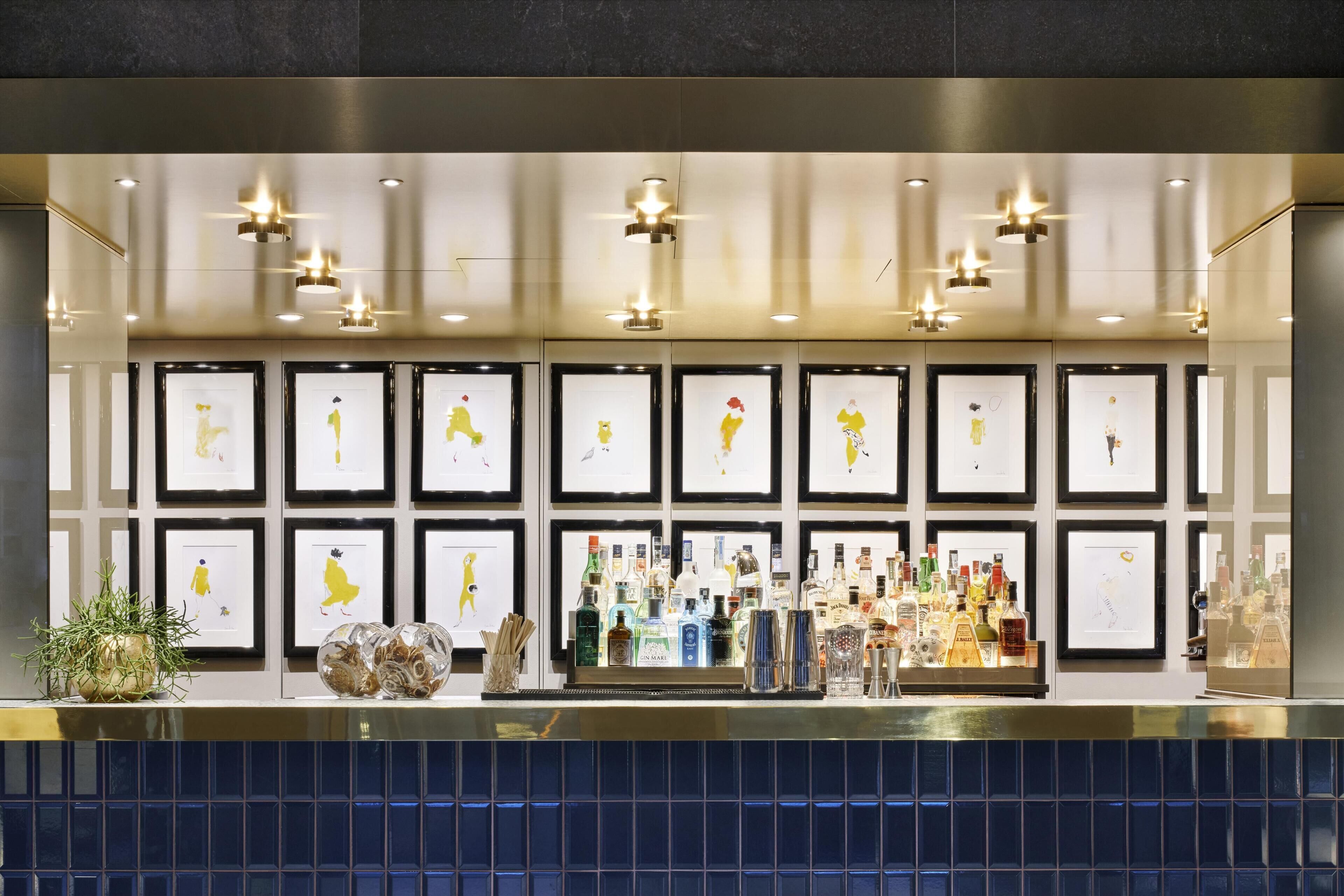 A bar area with framed artwork on the wall and a variety of liquor bottles on the counter.