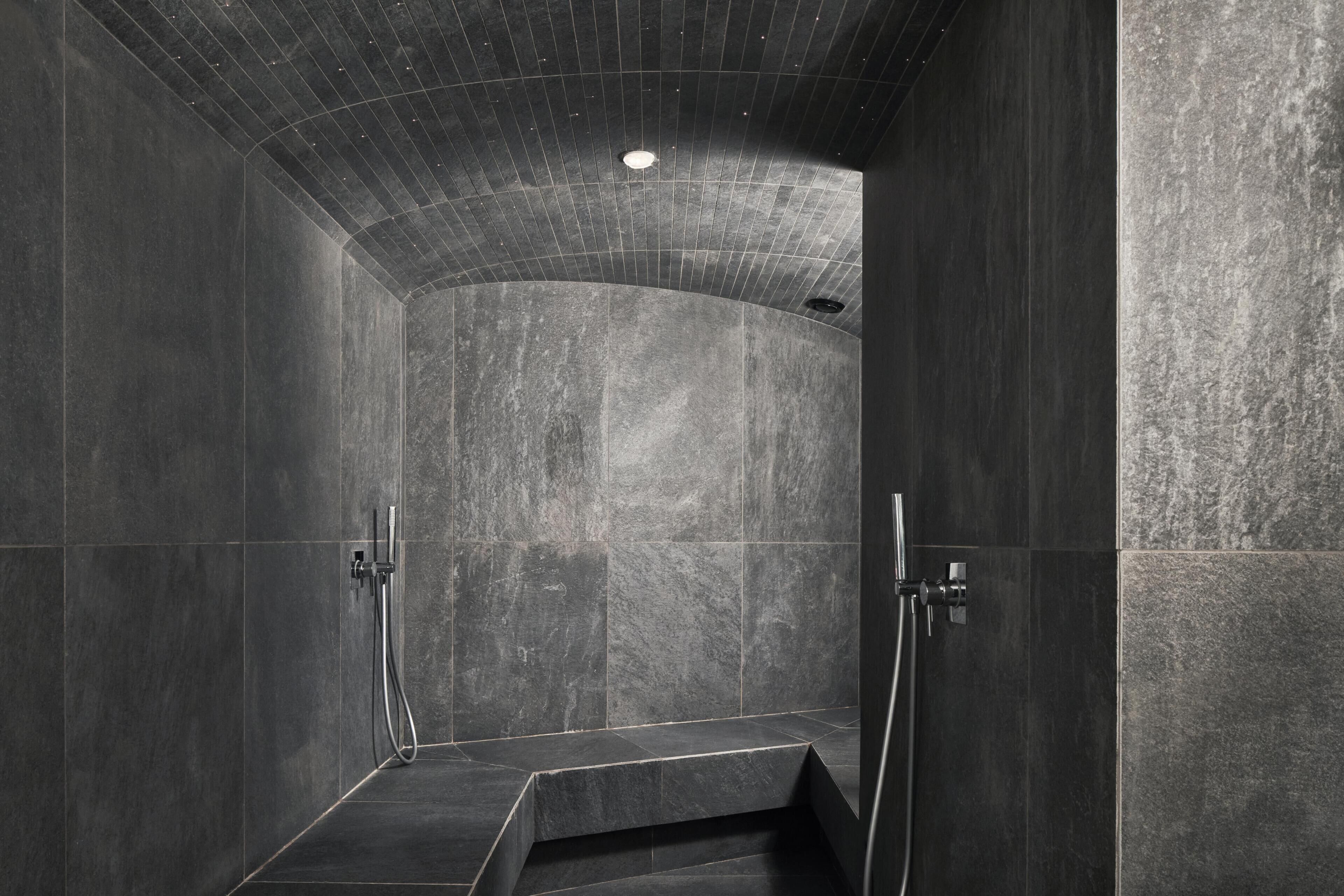 Een moderne douche met donkere tegels en een gebogen plafond.