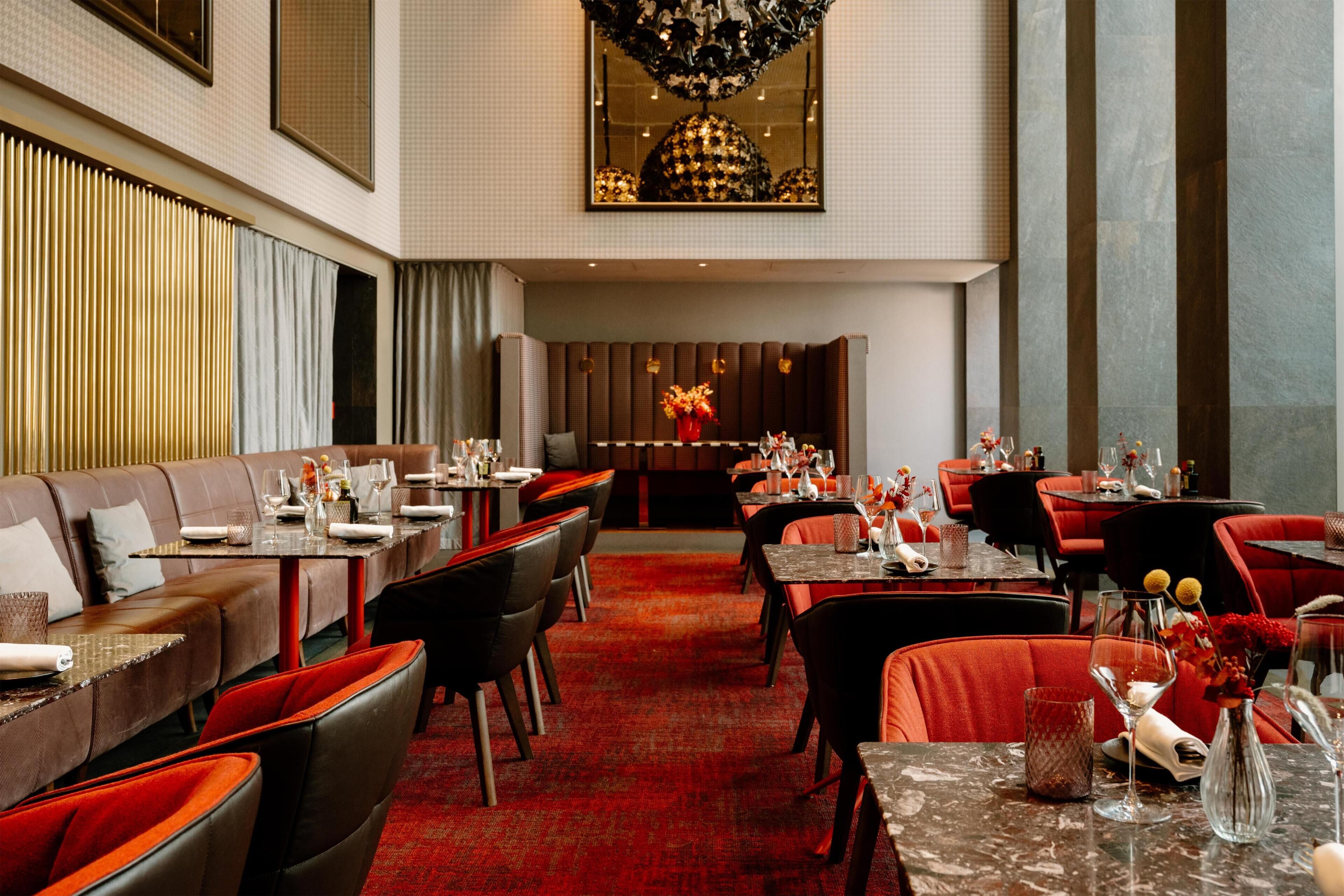 Un amplio vestíbulo de hotel con alfombra roja, asientos de cuero y mesas dispuestas para comer.