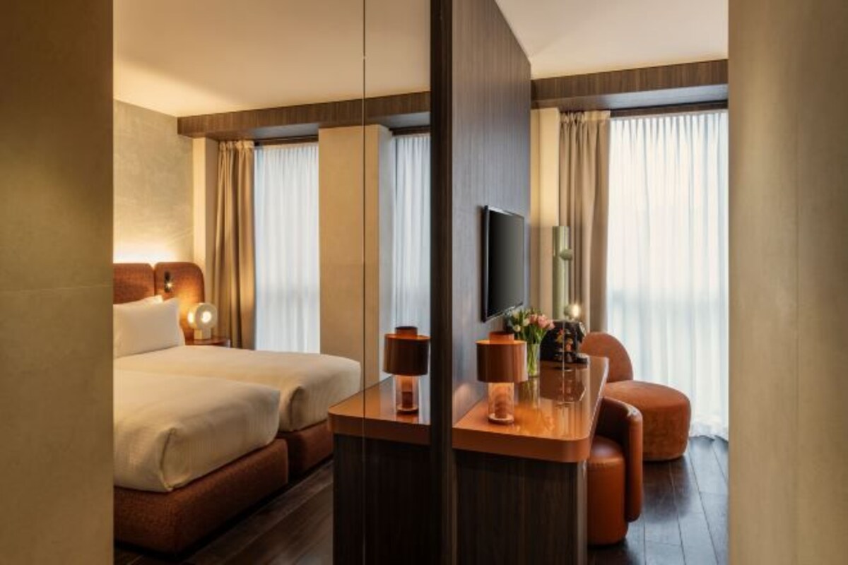 Una habitación de hotel con cama, escritorio, silla, televisor y espejo.