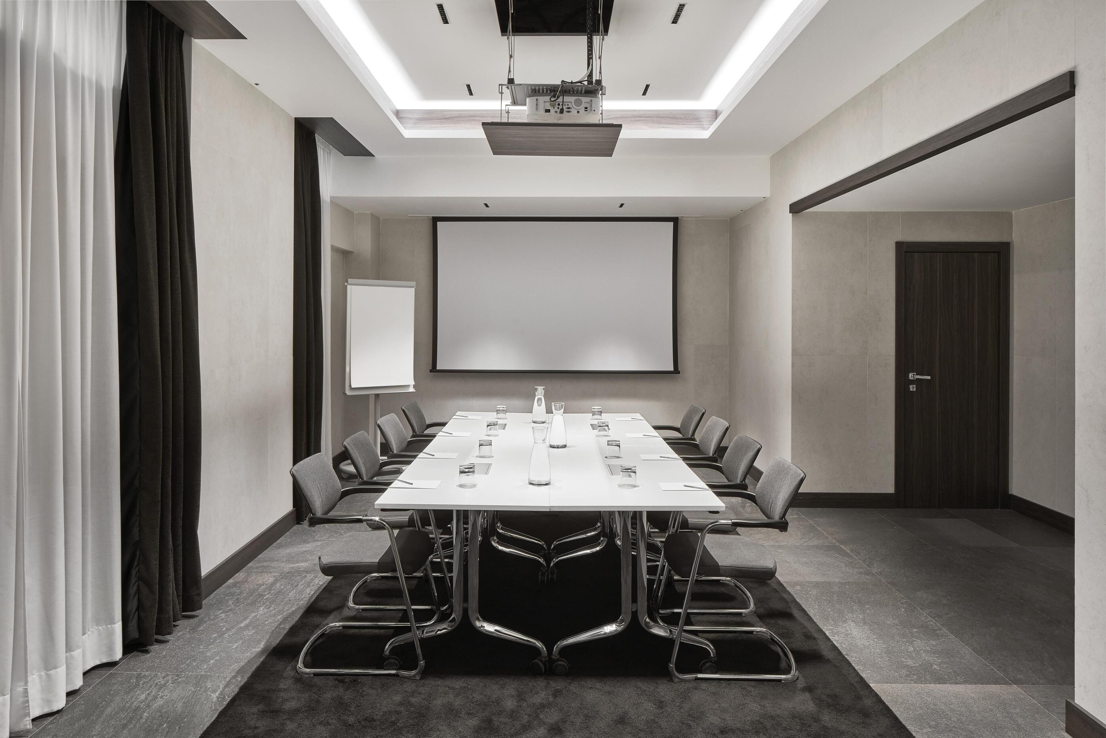 Uma sala de conferências com uma mesa grande, cadeiras, uma tela de projetor e um quadro branco.
