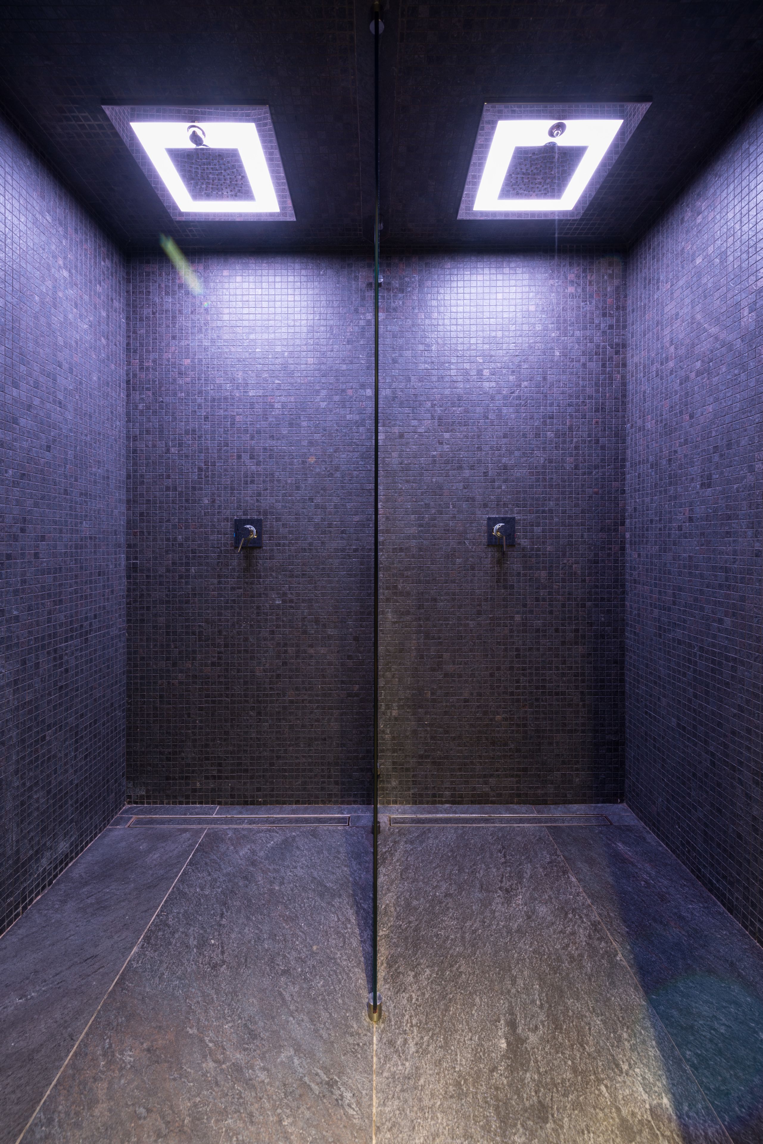 A tiled bathroom with two square ceiling lights and two wall-mounted faucets.